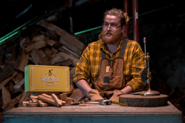 A man sits in his workshop with a box of Hot Box Cooking Wood