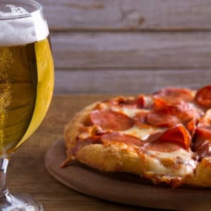 A glass of beer and pepperoni pizza on a wooden table