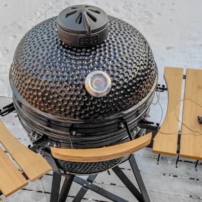 A kamado grill with a thermometer next to it.