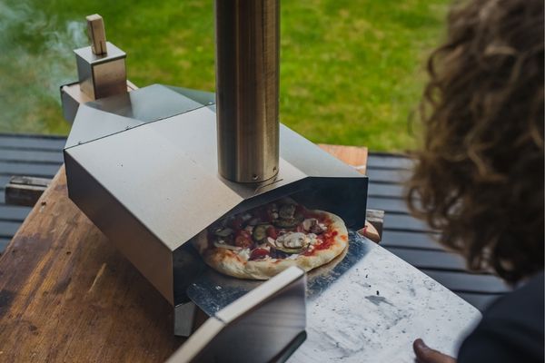 Person rotating a pizza in a portable pizza oven
